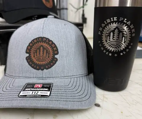 Matching grey snapback hat and black tumbler engraved with a Prairie Plains logo