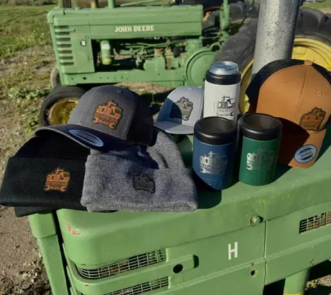 Custom hats and insulated bottles arranged on a green tractor hood outdoors